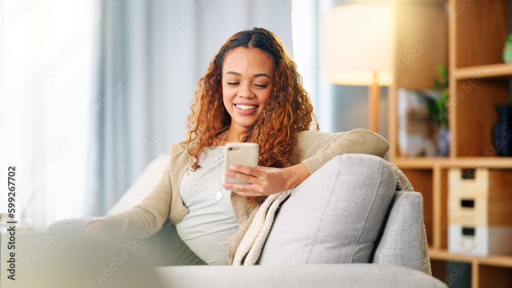 Wall mural Young woman smiling and laughing while texting on a phone at home. Cheerful female chatting to her friends on social media, browsing online and watching funny internet memes while relaxing on a sofa