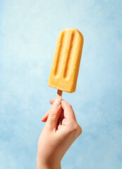 Woman hand holding yellow fruit popsicle on blue background