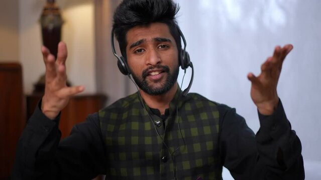 Web chat portrait of confident handsome young freelancer talking looking at camera gesturing. Front view medium shot of Middle Eastern man in headphones messaging online from home office