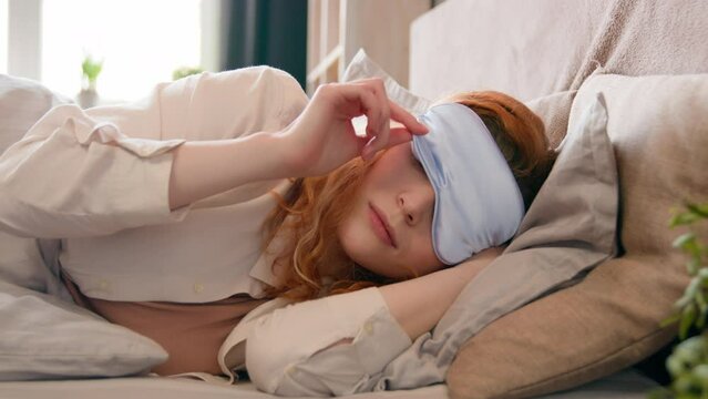 Sleepy beautiful woman waking up lying in comfortable white bed peeks out from under sleep mask opens eye happy smile fall asleep again girl female early good morning napping in cozy bedroom lazy lady
