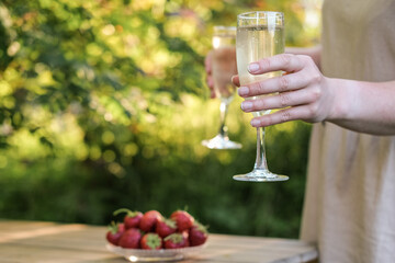 Glasses of champagne in female hands in a summer garden against the backdrop of evening sunlight