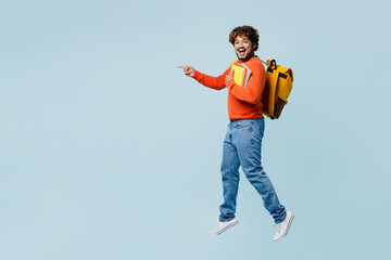 Full body sideways fun young teen Indian boy student wear casual clothes backpack bag hold books jump high point finger aside isolated on plain blue background. High school university college concept.
