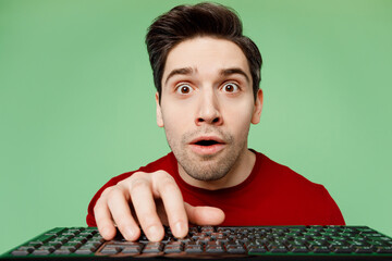 Close up programmer shocked surprised young IT man he wears red t-shirt casual clothes typing on pc computer keyboard isolated on plain pastel light green background studio portrait Lifestyle concept