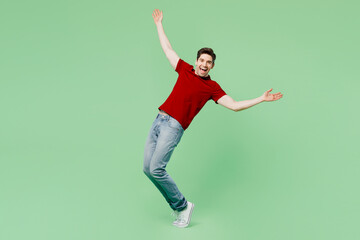 Full body side view young man he wears red t-shirt casual clothes stand on toes leaning back with outstretched hands isolated on plain pastel light green background studio portrait. Lifestyle concept.