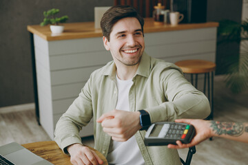 Young man wear casual clothes sit alone at table in coffee shop cafe restaurant indoors work or study on laptop pc computer hold bank terminal to process acquire smart watch payment Freelance concept