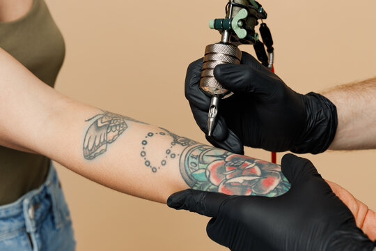 Cropped close up photo of tattooer master artist tattooed man wears black sterile gloves hold machine black ink in jar, equipment for making tattoo art on body hand isolated on plain beige background.