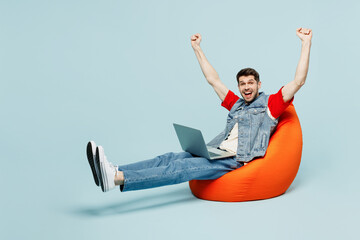 Full body young IT man he wear denim vest red t-shirt casual clothes sit in bag chair hold use work...