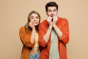 Young shocked scared fearful couple two friends family man woman wear casual clothes looking camera biting nails fingers together isolated on pastel plain light beige color background studio portrait. - obrazy, fototapety, plakaty