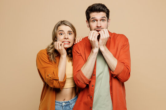 Young shocked scared fearful couple two friends family man woman wear casual clothes looking camera biting nails fingers together isolated on pastel plain light beige color background studio portrait.