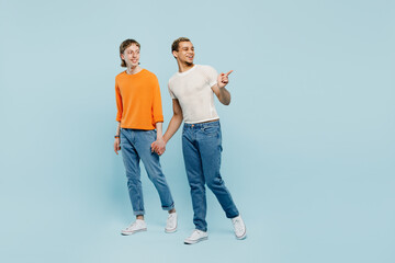 Obraz premium Full body sideways young couple two gay men wear casual clothes together walk go hold hands point aside isolated on pastel plain blue color background studio. Pride day june month love LGBTQ concept.