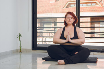 young plus size latina woman sitting indoors meditating doing anjali mudra position