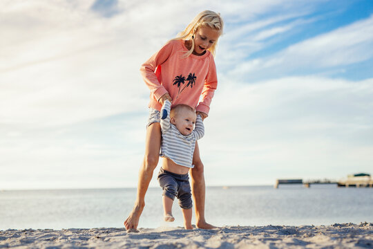 Older sister (8-9) teaching baby sister (6-11 months) to walk on beach