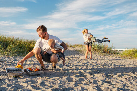 Parents with children (6-11 months, 4-5) barbecuing on beach