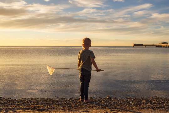 Boy (4-5) fishing in sea at sunset