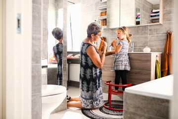Grandmother and granddaughter (2-3) brushing teeth in bathroom