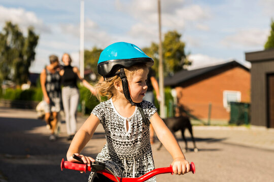 Girl (2-3) riding bicycle, family in background