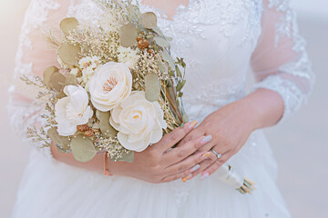Bride woman holding a bouquet of white flowers in hand, close-up photo.