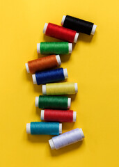 Multicolored yarn on spool for sewing on a yellow background. Top view.
