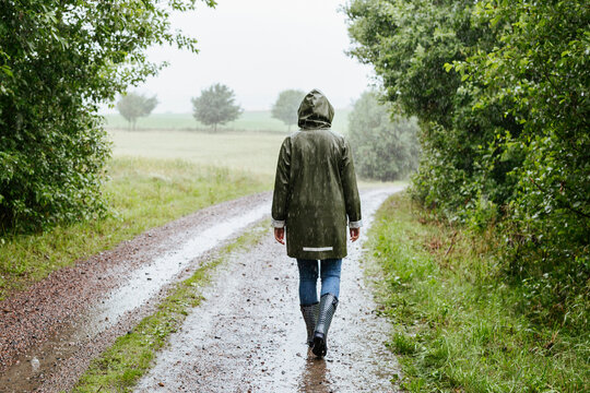 Rear view of woman in green raincoat walking in rain