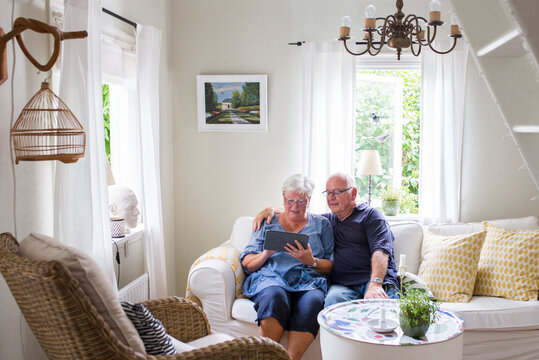 Senior woman and man sitting on sofa and using digital tablet