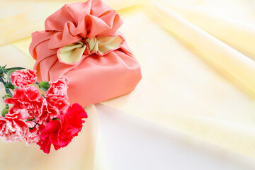 ピンクの風呂敷でラッピングしたギフトと花　贈り物のイメージ