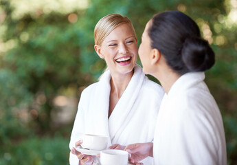 Best friends and beauty remedies. Two young women having coffee in their bathrobes at the day spa.