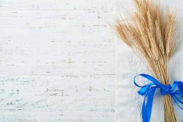 Shavuot jewish holiday celebration. Bouquet of golden ripe wheat with blue ribbon. White wood board table with field of wheat. Background for Shavuot celebration. Top view. Mock up.
