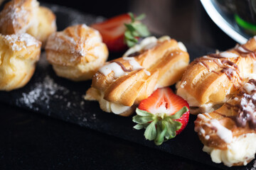 Pastry background. Confectionery closeup. Black marble exclusive food background. Sweets isolated on stone. Sweet cake powder sugar sprinkle. Eclair dessert. Delicious chouquette.