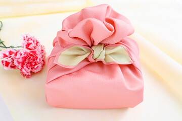 ピンクの風呂敷でラッピングしたギフトと花　贈り物のイメージ