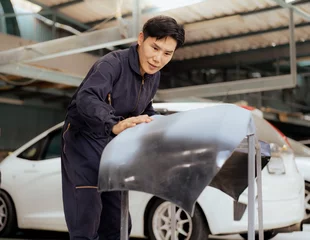 Deurstickers Auto mechanic examining automobile body front bumper before put it on damaged car at auto repair service station. Asian repairman fixing vehicle bumper broken from collision crash accident on road. © Nassorn