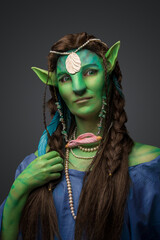 Portrait of fairytale druid woman with green skin dressed in jewelry and gown.