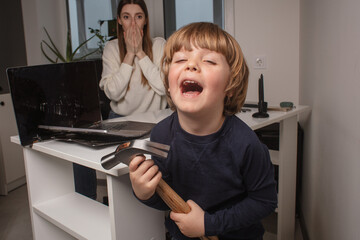 Happy child smashes mom's work laptop to spend more time together. The toddler laughs because he...
