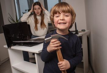 Happy child smashes mom's work laptop to spend more time together. The toddler laughs because he...