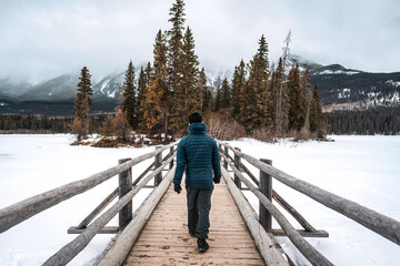 A man walking on wooden bridge among frozen lake in Pyramid Lake on winter at Jasper national park