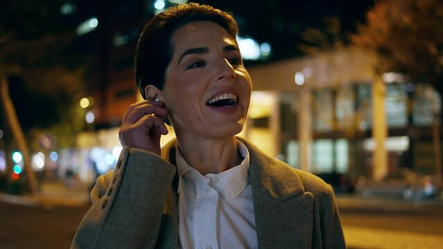 Closeup night woman talking in earphones. Smiling businesswoman plug in earpods