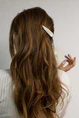 Young blond woman from behind with long loose wavy hair, clipped with pearly snap hair clip.