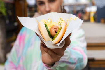 Young Slim brunette girl eating fast food hotdog or burger outdoor on the street.