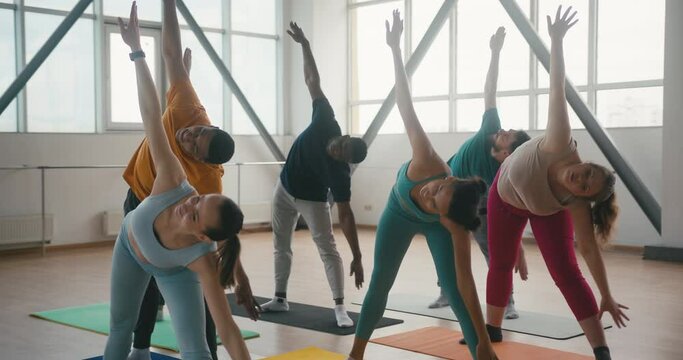 People repeat triangle pose after coach during yoga class