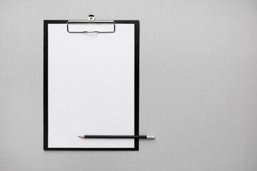Photo of clipboard with a blank sheet of paper and pencil on gray paper background. Copy space for text. Flat lay.