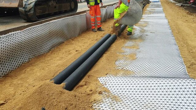 Groundworkers installing new electric ducts during roadworks on construction site