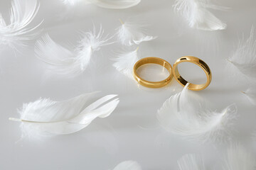 Two gold rings on white glass and many feathers around
