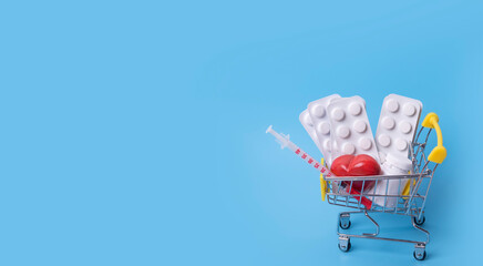 Various tablets, medicine, heart and injector in shop trolley on a blue background. Idea for health care, health insurance and diabetic medications. Buy and shopping medicine concept. Copy space. © Iryna