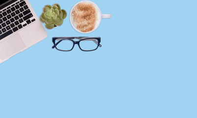 Top view workspace on blue background with laptop, plant, coffee, glasses. Space for text. The...