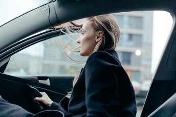 Woman in black coat get out from the car in the city. Windy weather, blowing hairs