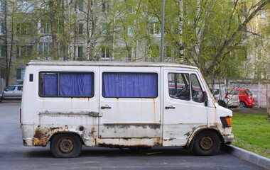 An old rusty white minibus is parked in the courtyard of a residential building, Belysheva Street, St. Petersburg, Russia, May 2023