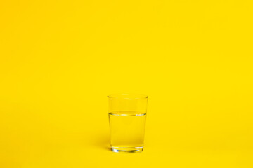 Vaso de agua de cristal sobre fondo de estudio amarillo