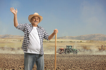 Mature farmer with a shovel standing on a field with a tractor