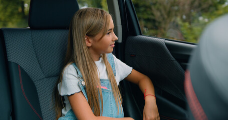 Fototapeta na wymiar Attractive positive calm blond teen girl sitting in the car and observes nature through the car window