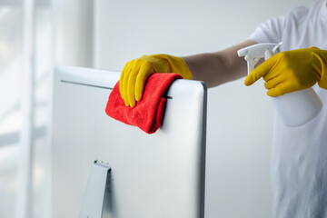 Person cleaning room, cleaning worker is using cloth to wipe computer screen in company office room. Cleaning staff. Concept of cleanliness in the organization.