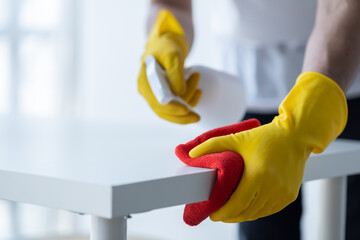 Person cleaning the room, cleaning staff is using cloth and spraying disinfectant to wipe the table in the company office room. Cleaning staff. Maintaining cleanliness in the organization.